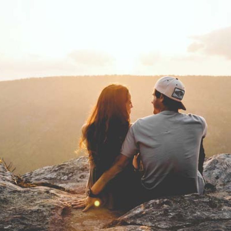 romantic couple sitting on rocks at sunset