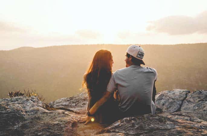 romantic couple sitting on rocks at sunset