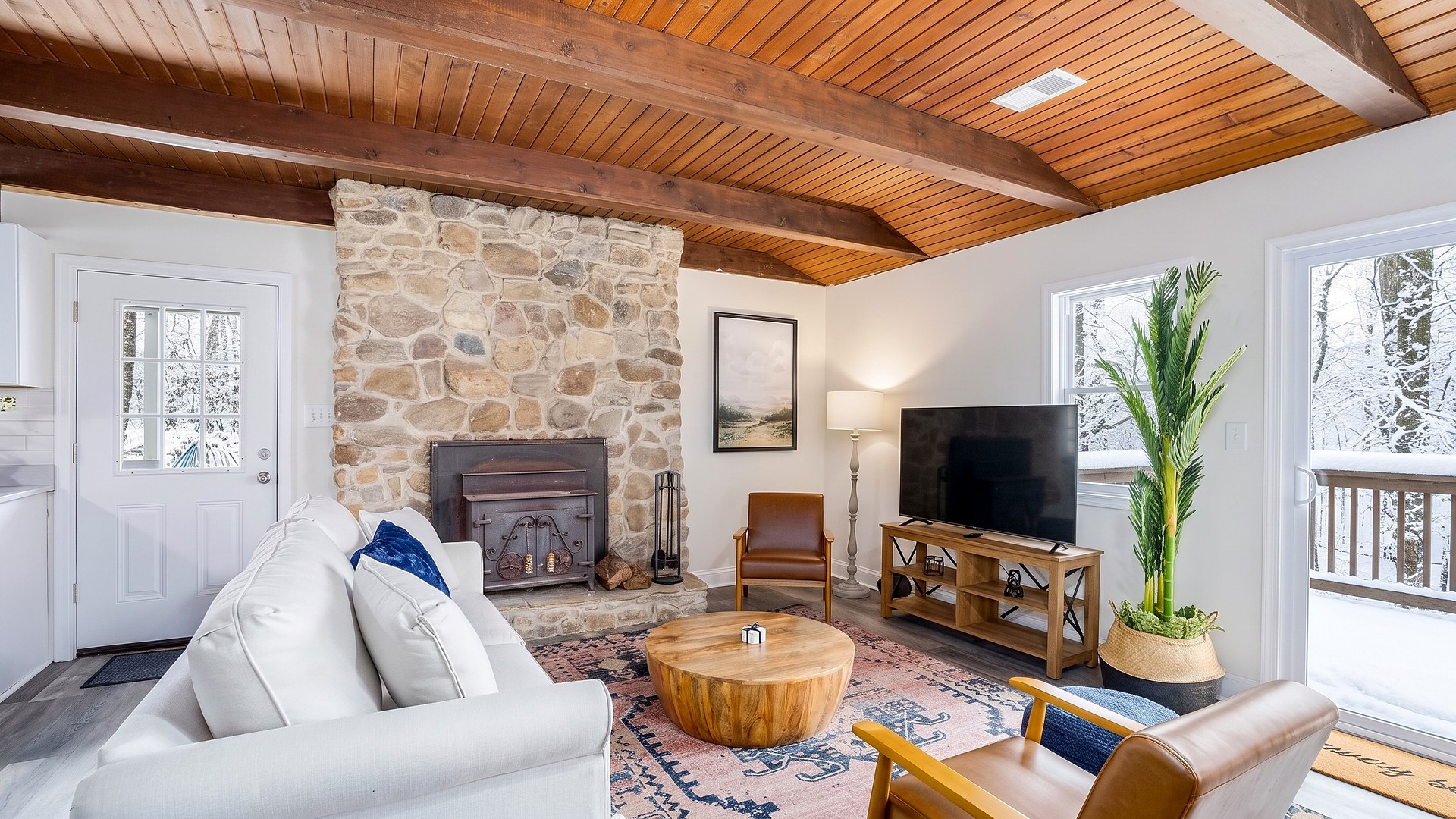 Living room with a stone fireplace and snowy winter views at Wildwood Chalet, a Blue Maple cabin